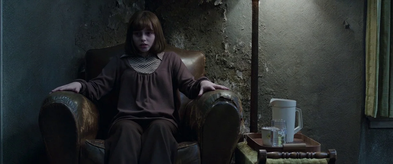 The Conjuring 2 (2016) movie still: medium — A dimly lit room features walls with decaying, peeling wallpaper and cracked plaster surfaces. A young…