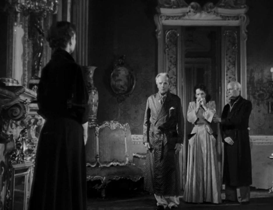 Roman Holiday (1953) movie still: fullbody — A dark, ornate room with classical wall molding and a large decorative fireplace. Three people stand…
