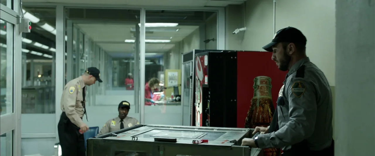 Den of Thieves (2018) movie still: medium — A utilitarian room features glass partitions, a red beverage vending machine, and grey walls. A security…