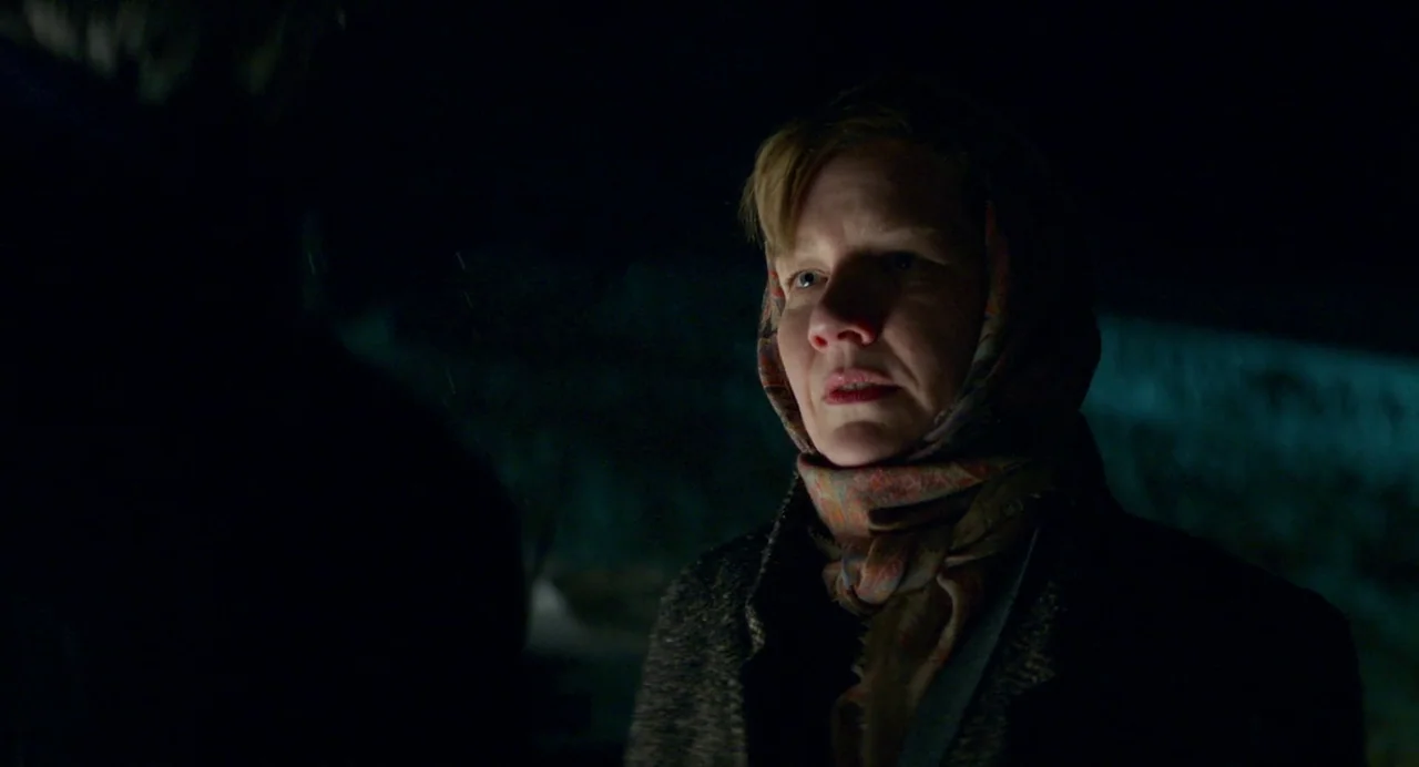 Anatomy of a Fall (2023) movie still: medium — A woman stands outdoors in a dark, cold environment with snow faintly visible. She wears a headscarf…