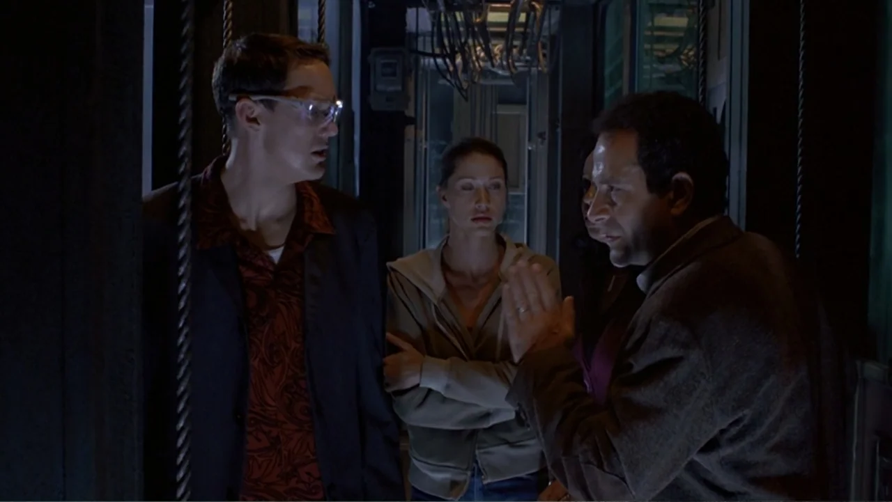13 Ghosts (1960) movie still: medium — A dimly lit elevator car with metallic walls and visible overhead cables. Three adults stand together in a…