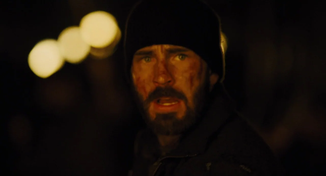 Snowpiercer (2013) movie still: closeup — A dark environment with out-of-focus golden lights in the background. A man with a bruised face looks into…