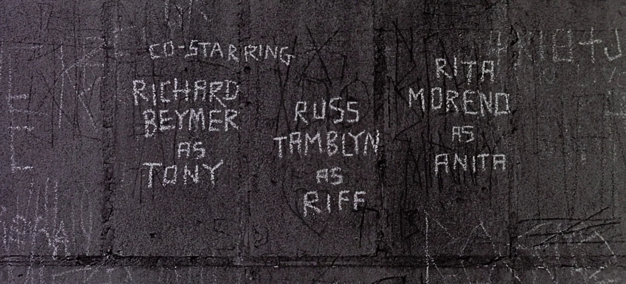West Side Story (1961) movie still: closeup — A dark concrete wall features rough white lettering inscribed across its textured surface. The text…