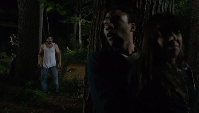 Mystery Team (2009) movie still: medium — A dark, densely wooded area serves as the backdrop for a tense nocturnal encounter. A man and woman stand…