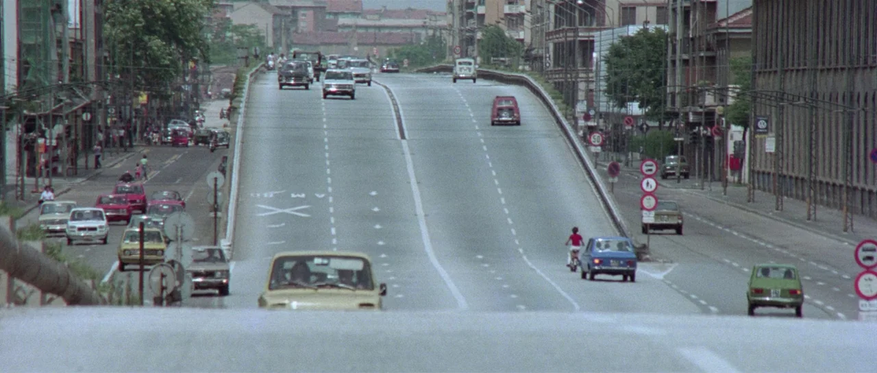 The Suspicious Death of a Minor (1975) movie still: establishing — An elevated overpass road stretches toward the center horizon with urban…