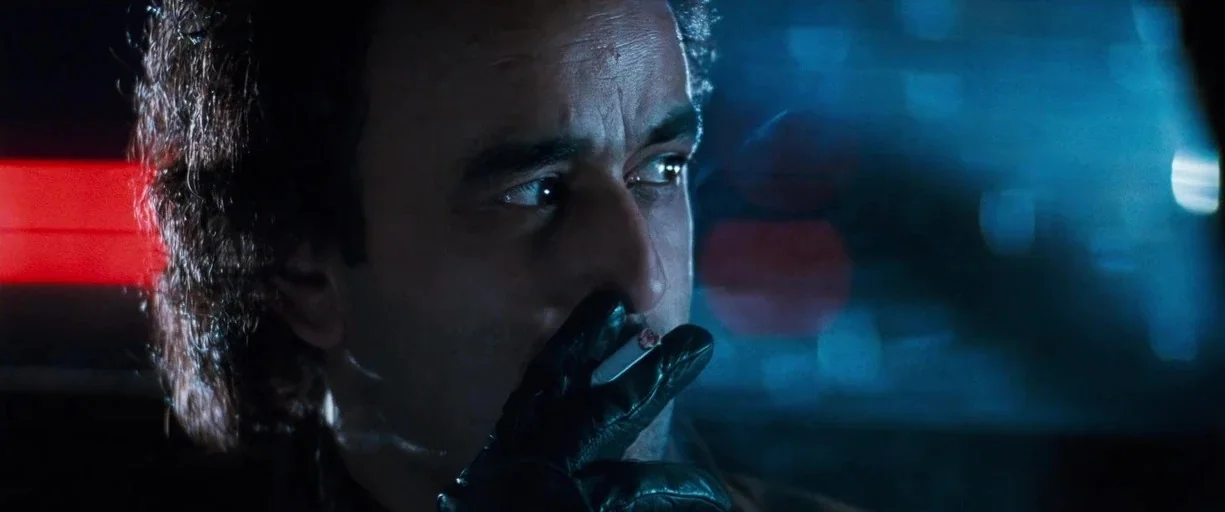 True Lies (1994) movie still: closeup — A dark vehicle interior with a glowing blue dashboard and a red light strip. A man wearing leather gloves…