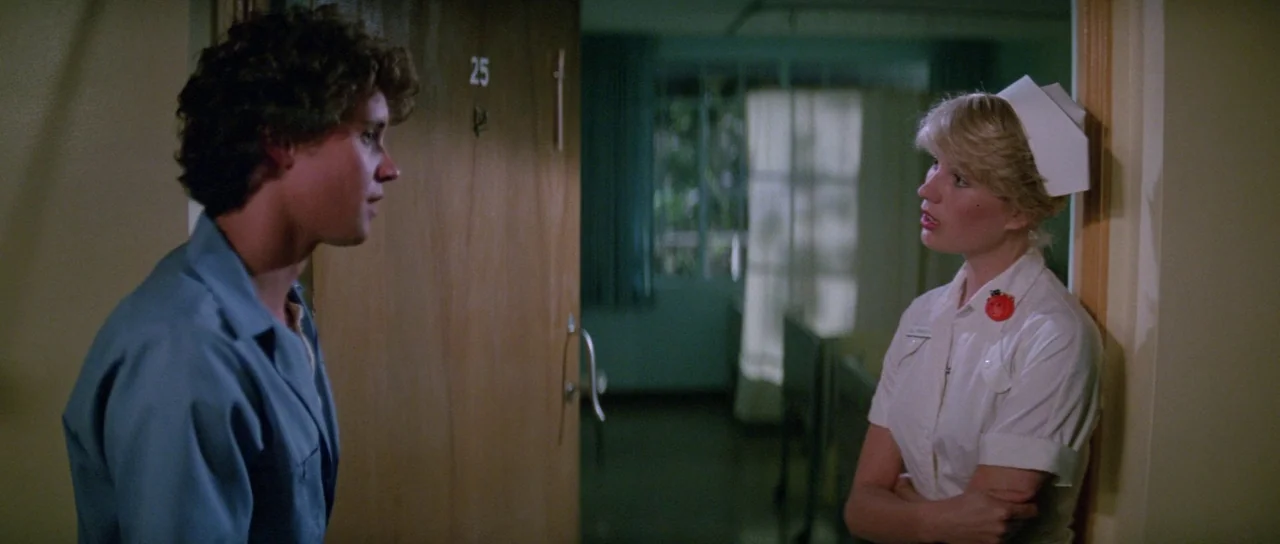 Halloween II (1981) movie still: medium — A hospital hallway with wood-paneled doors and a view into a patient ward. A man in a blue shirt faces a…