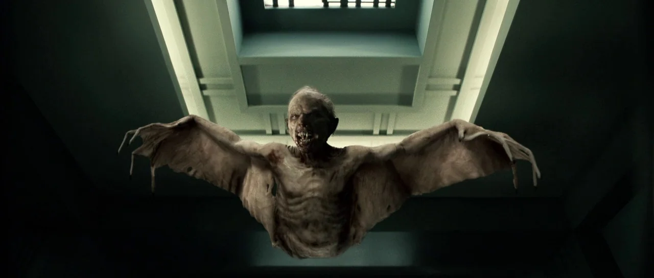 Daybreakers (2009) movie still: medium — A pale, winged creature hovers in the center of a dim, institutional-style hallway. The creature spreads…