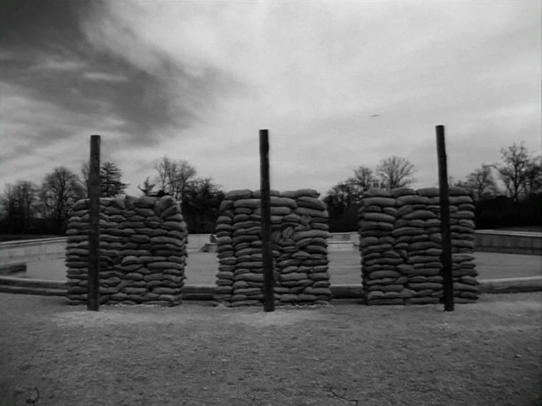 Paths of Glory (1957) movie still: wide — An outdoor area with three tall wooden posts standing before individual sandbag walls. The setting…