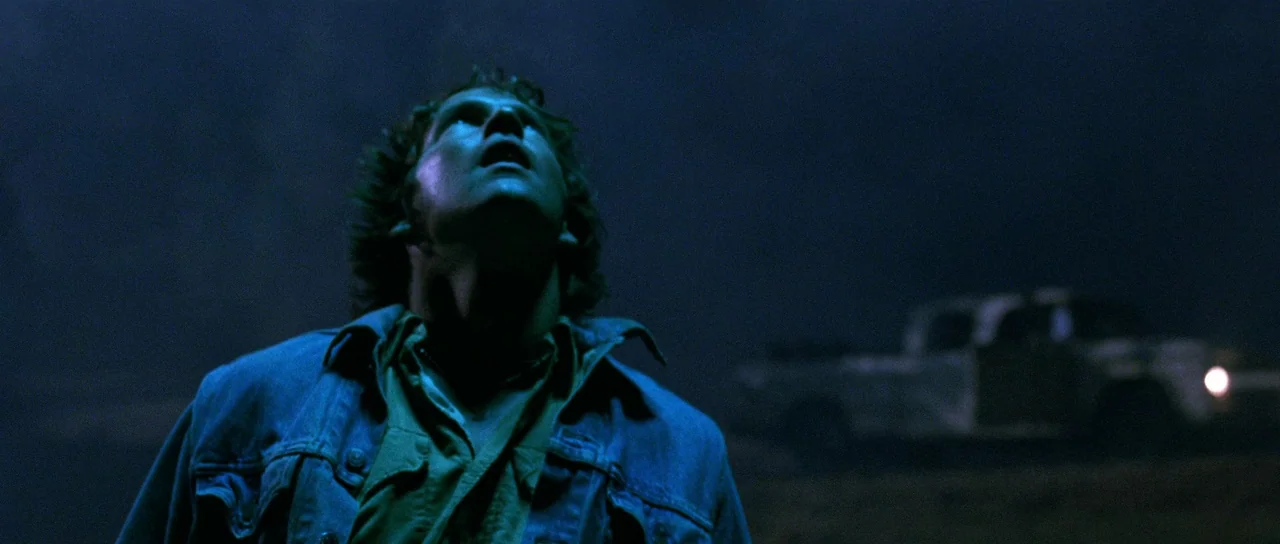 Fire In The Sky (1993) movie still: medium — A dark, empty landscape at night with a blurred pickup truck in the background. A man stands in the…
