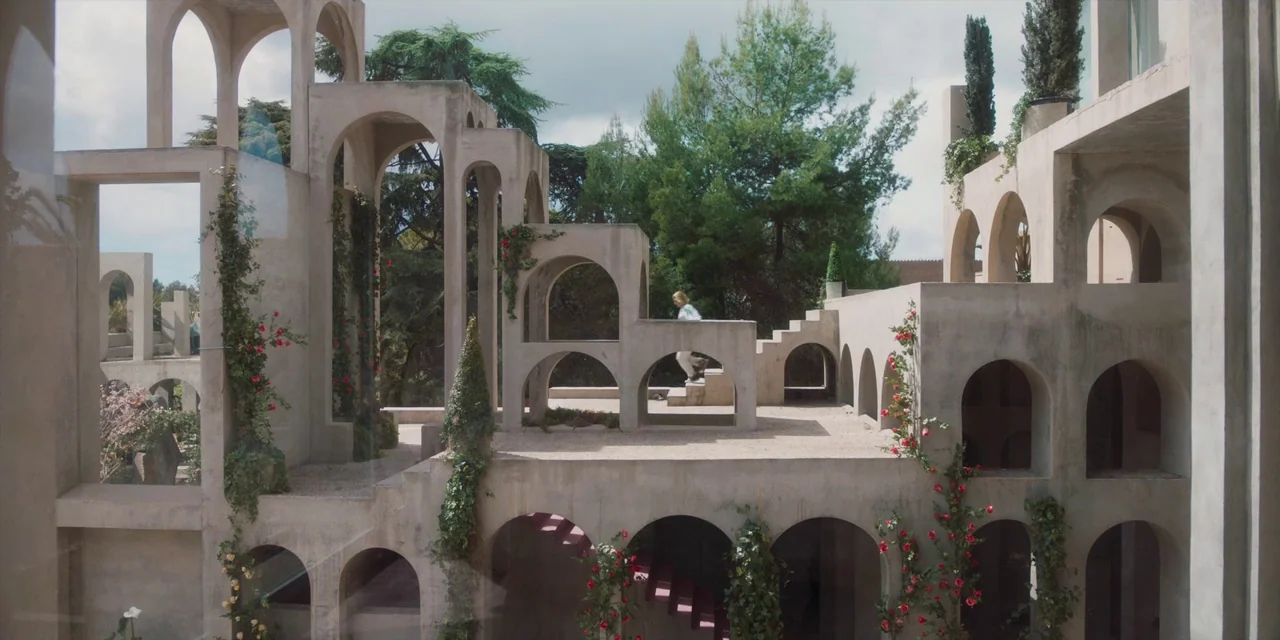 Paradise Hills (2019) movie still: wide — A sprawling outdoor architectural complex features interlocking concrete arches and tiered gravel levels.…