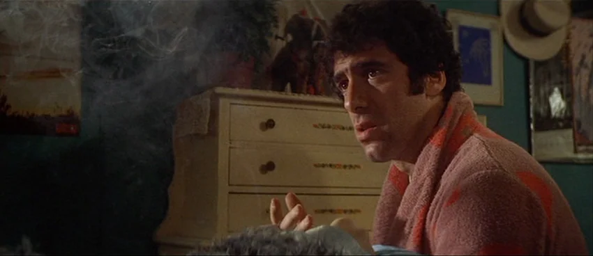 California Split (1974) movie still: medium — A dimly lit bedroom features a wooden dresser with small decorative patterns. A man in a pink bathrobe…