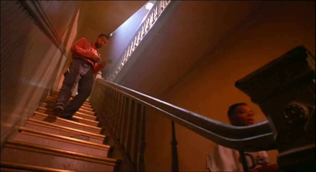 Do The Right Thing (1989) movie still: fullbody — A wooden staircase with a banister in a multi-story building. A man in a red shirt walks down the…