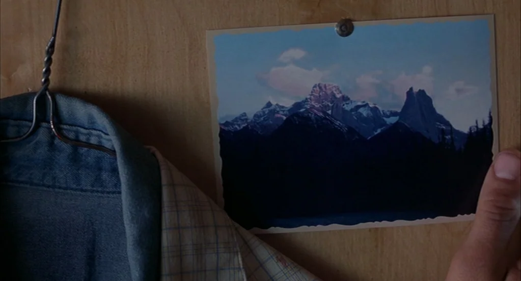 Brokeback Mountain (2005) movie still: closeup — A wooden closet door with a photograph of a mountain range pinned to it. A person's hand reaches…