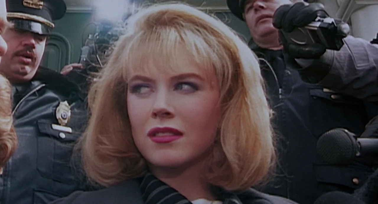 To Die For (1995) movie still: closeup — A woman stands in a crowd of people holding cameras and recording equipment outdoors. She gazes slightly to…