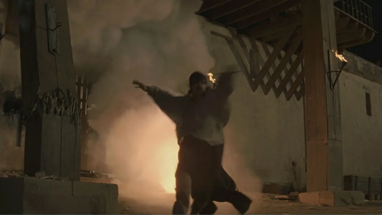 The Mask of Zorro (1998) movie still: fullbody — A stone courtyard at night features wooden structures and thick, billowy white smoke. A man jumps…