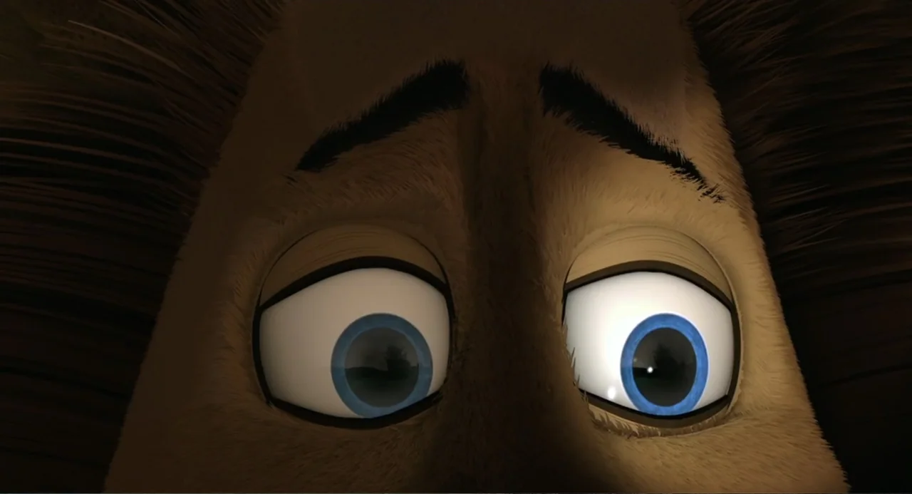 Madagascar (2005) movie still: closeup — A close up view focuses on the eyes and brow of a furry creature in darkness. The character looks down with…