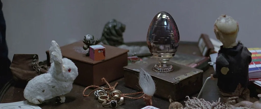Let The Right One In (2008) movie still: medium — A cluttered tabletop holds a collection of small toys and decorative trinkets. A polished metallic…