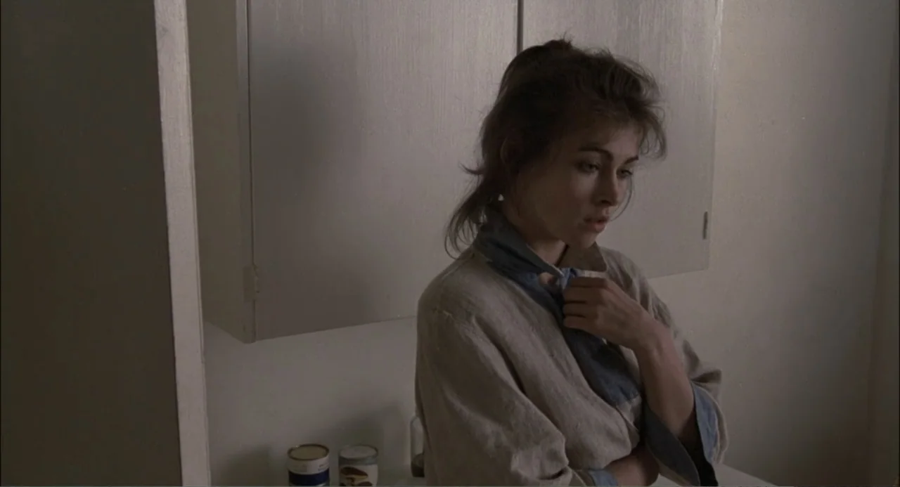 Gorky Park (1983) movie still: medium — A dimly lit interior space features off-white cabinetry and plain walls. A woman in a robe stands near the…