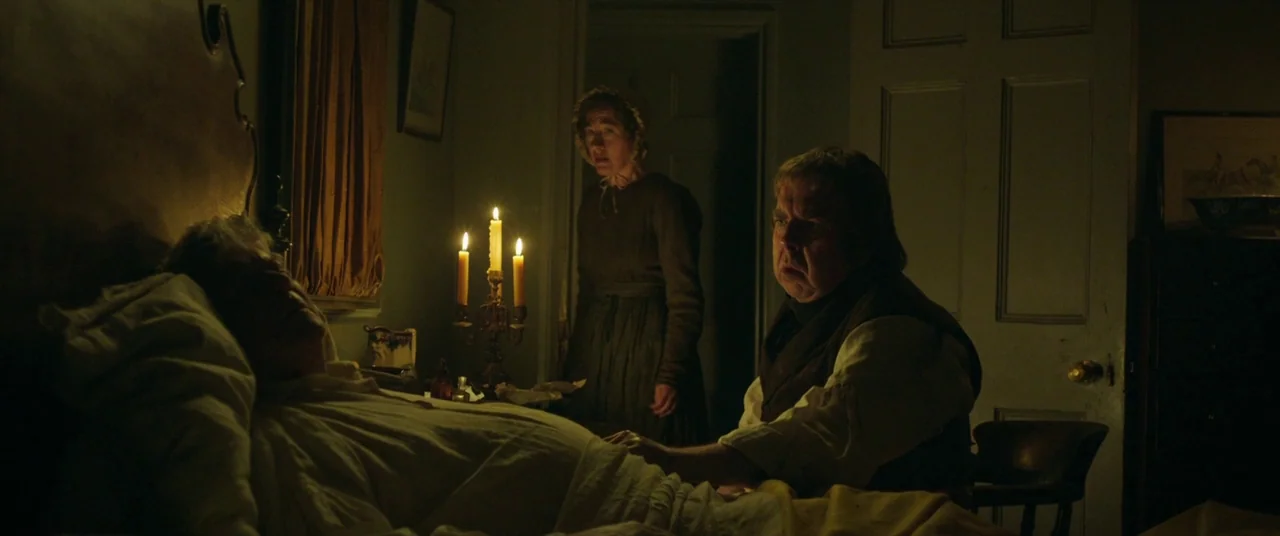 Mr. Turner (2014) movie still: medium — A dimly lit 19th-century bedroom features a sick person lying in a wooden bed. A man and woman in period…