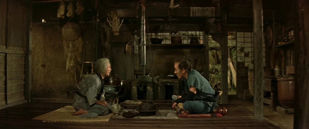 Ballad Of Narayama (1958) movie still: wide — A rustic, wooden Japanese interior features a central fire hearth and woven straw mats. An elderly…
