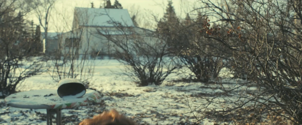 The Best Christmas Pageant Ever (2024) movie still: establishing — A snowy backyard with bare bushes and a white house in the background. A small…