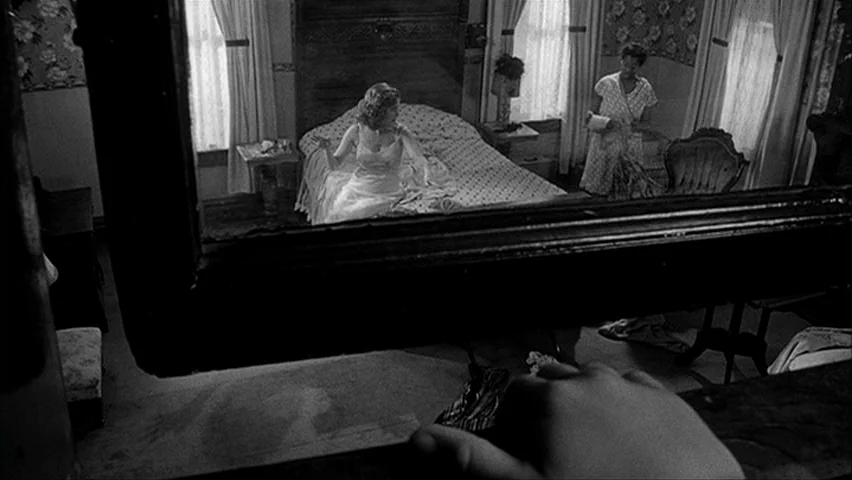 Paper Moon (1971) movie still: medium — A 1940s room features floral wallpaper, a patterned bedspread, and two large curtained windows. A woman sits…