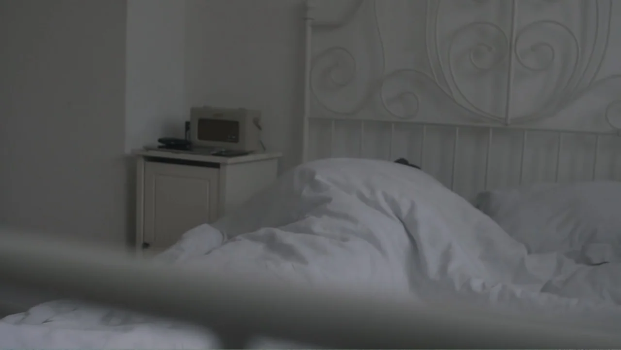 A Film Called Blacks Can't Swim (My Journey My Story) (2020) movie still: medium — A white metal bed frame holds a person tucked underneath a thick…