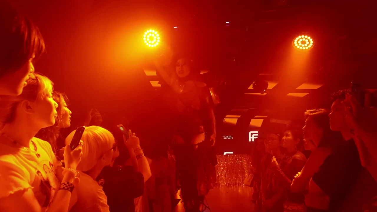 The Last Year of Darkness (2023) movie still: medium — A dark indoor nightclub stage is bathed in intense red light. A performer poses on stage…