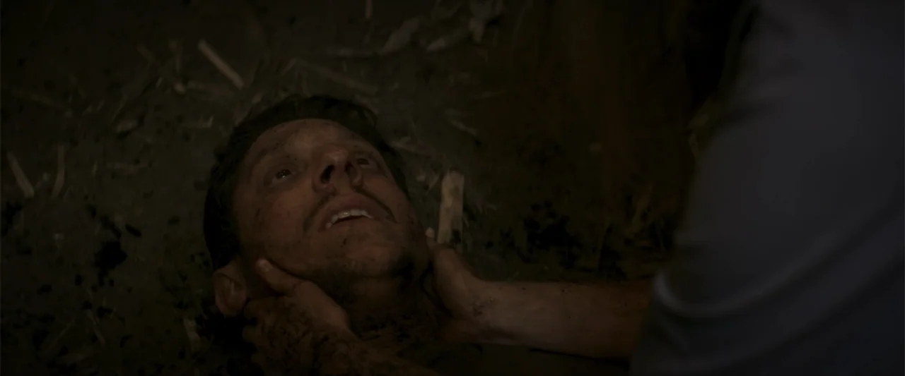 Treblinka's Last Witness (2012) movie still: closeup — A dark outdoor space with a ground surface covered in damp soil and debris. A person holds…