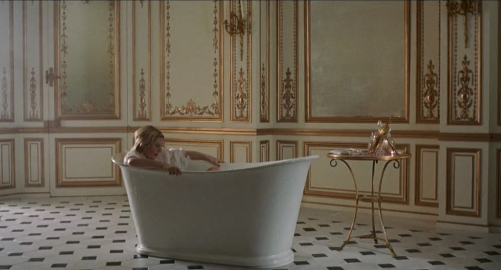 Marie Antoinette (2006) movie still: wide — An opulent bathroom features white paneled walls with gold molding and a checkered marble floor. A woman…