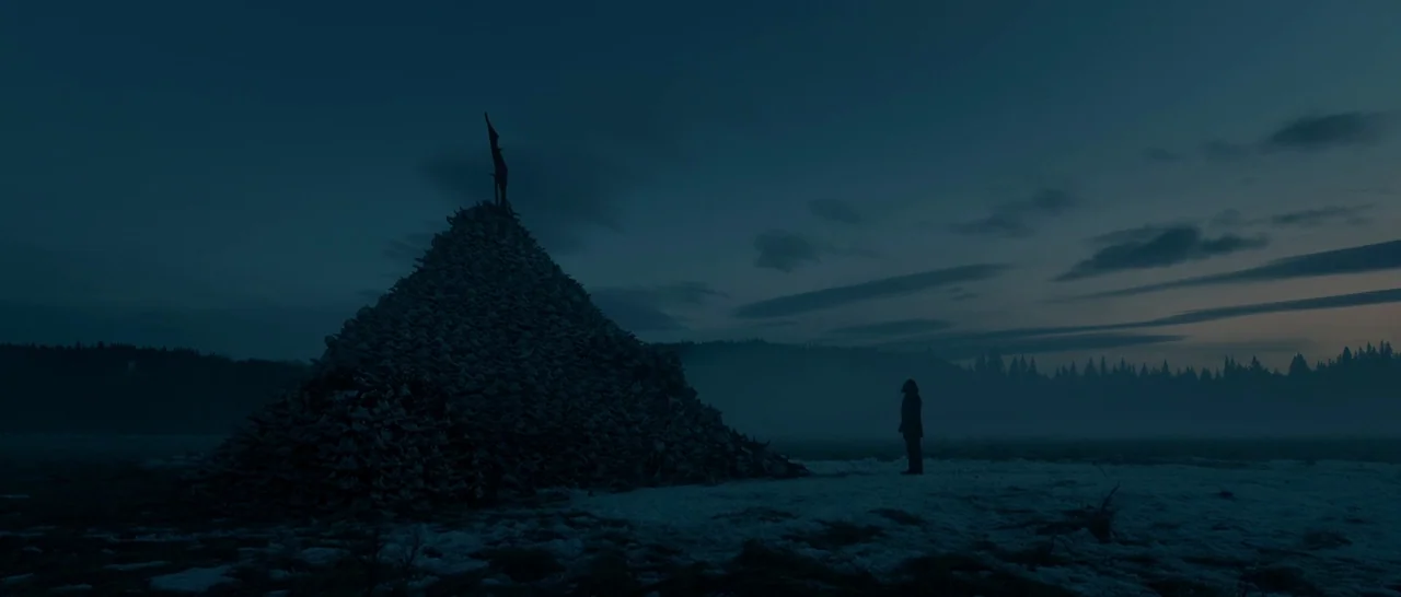 The Revenant (2015) movie still: wide — A dark, expansive field contains a massive, pointed pile of white animal skulls. A single figure stands in…