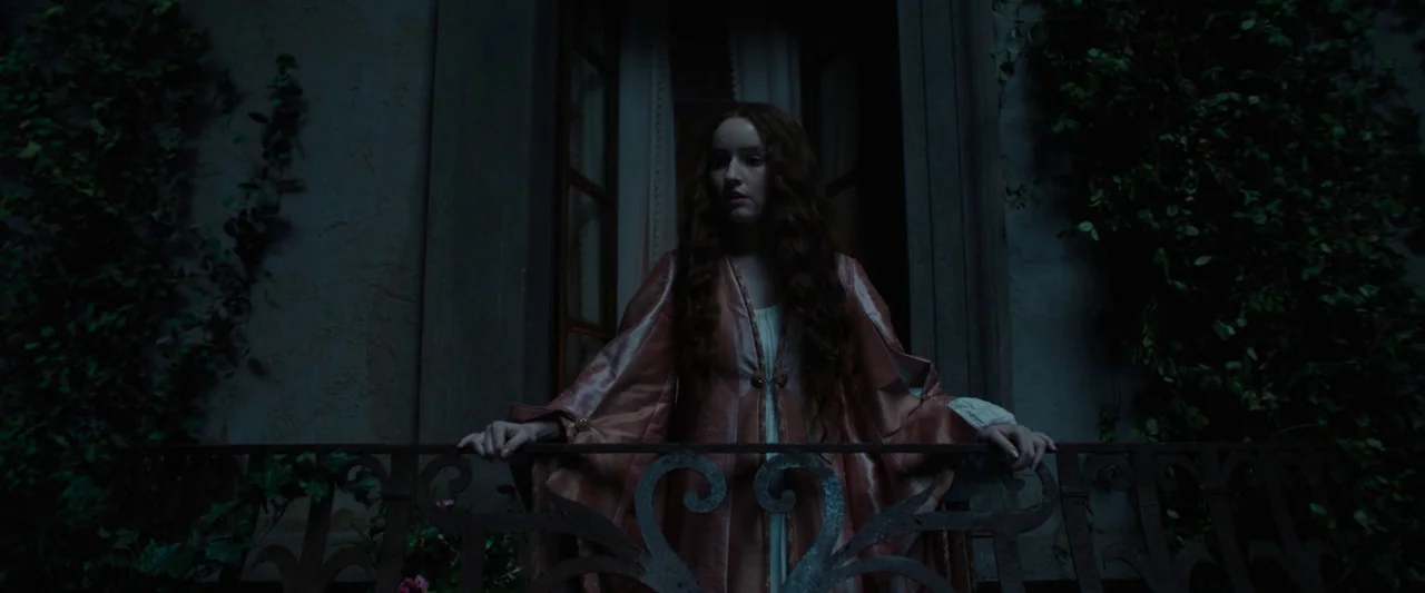 Rosaline (2022) movie still: medium — A stone balcony exterior at night with thick climbing ivy on the walls. A young woman with long red hair rests…