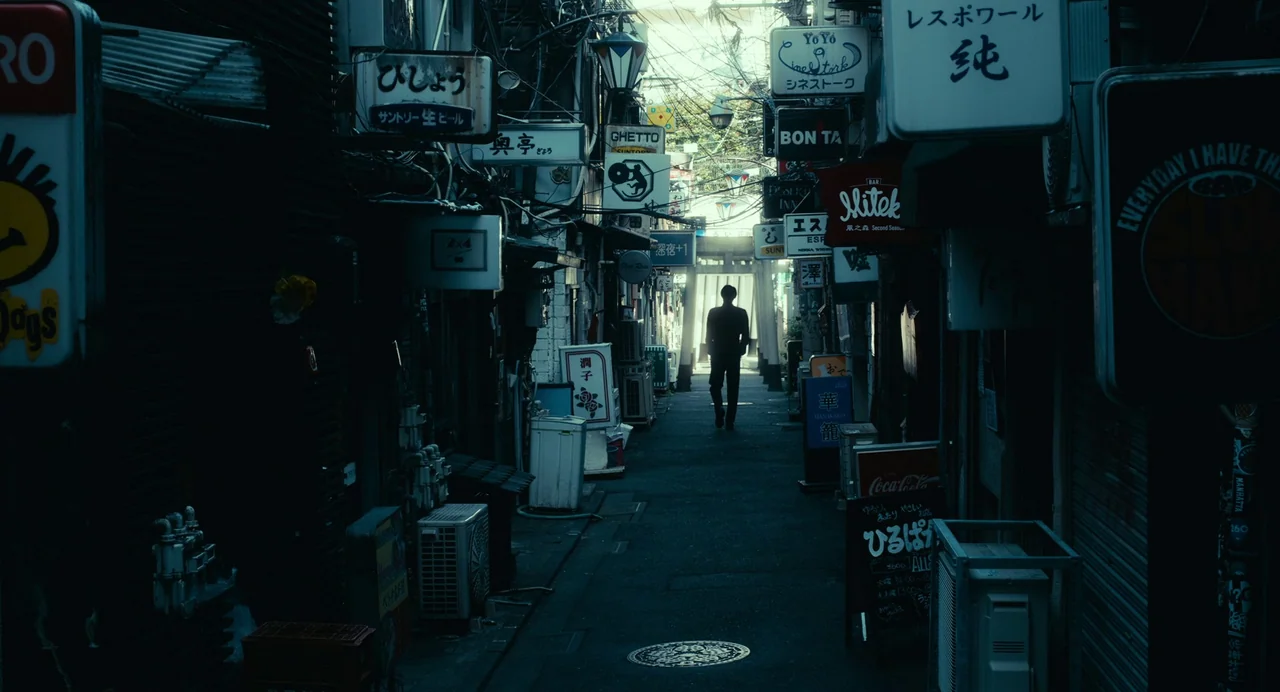 xxxHolic (2022) movie still: wide — A narrow Tokyo-style alleyway is densely packed with illuminated signs and cluttered electrical wires. A lone…