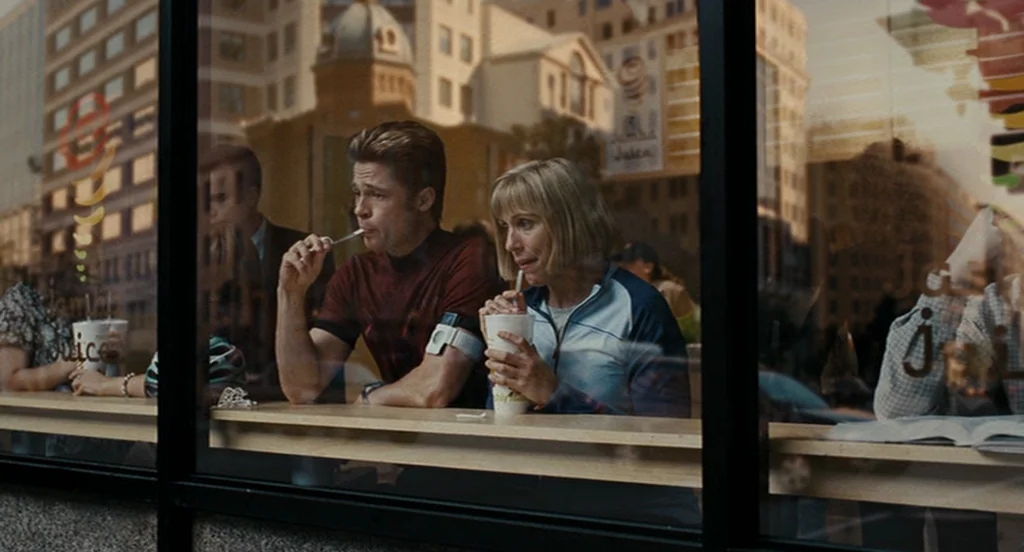 Burn After Reading (2008) movie still: medium — A window-facing bar in a public space features two people sitting together. They are holding plastic…