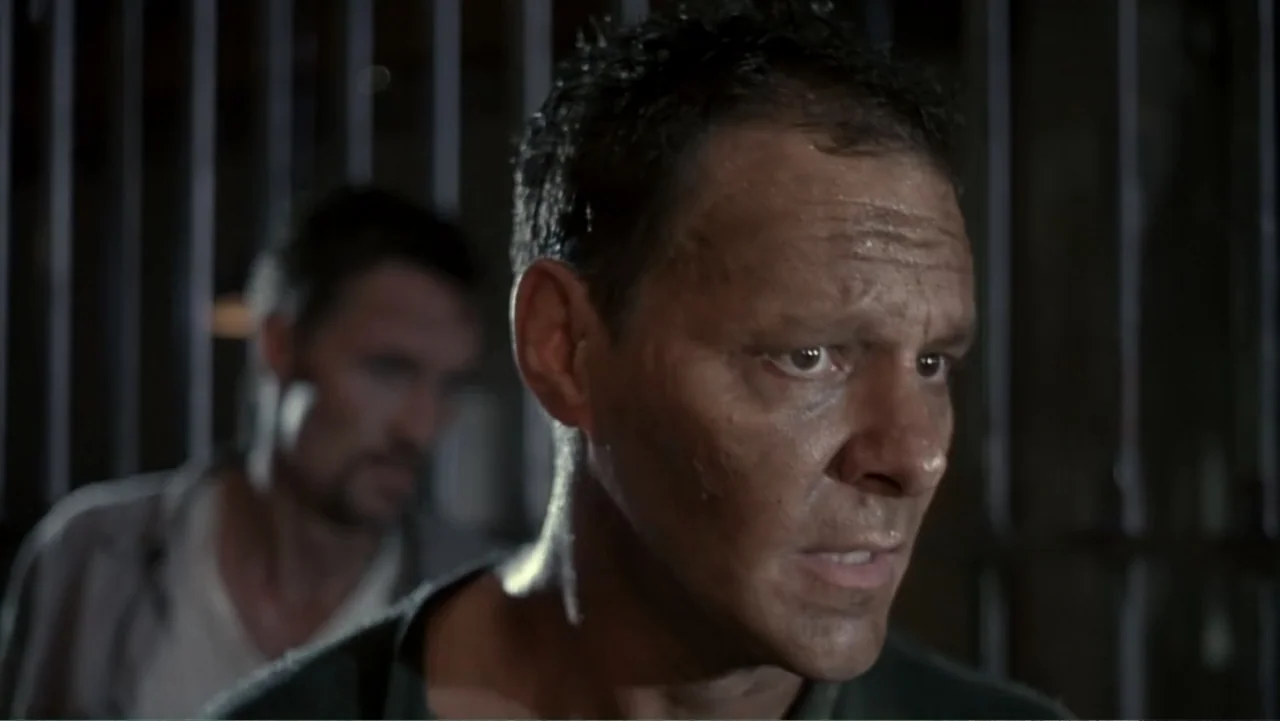 Behind Enemy Lines (2001) movie still: closeup — A dimly lit prison cell features a background of vertical iron bars. A man stands in the foreground…