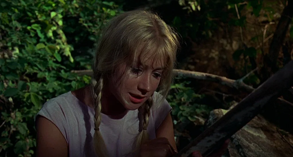 Age of Consent (1969) movie still: medium — A dense woodland environment with abundant green foliage in the background. A young woman with blonde…