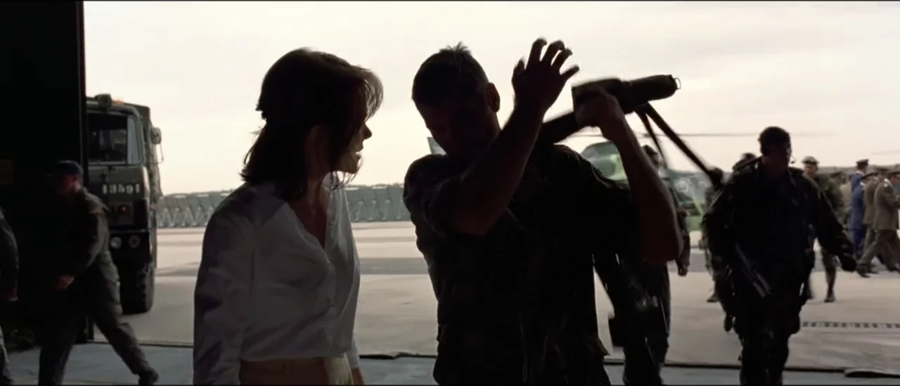 The Peacemaker (1997) movie still: medium — A spacious aircraft hangar with light pouring in from the exterior loading bay. A woman in a white shirt…