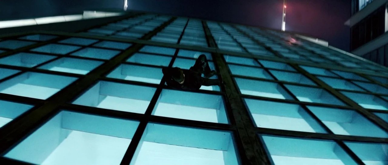 Mission: Impossible III (2006) movie still: wide — A dark, modern skyscraper wall is illuminated from behind by a grid of blue lights. A single…