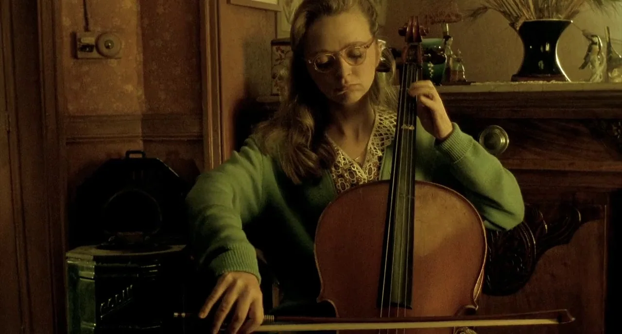 Delicatessen (1991) movie still: medium — A dimly lit room features a wooden fireplace mantel with decorative ceramic ornaments. A young woman in a…