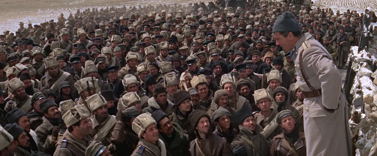 Doctor Zhivago (1965) movie still: wide — A vast crowd of soldiers wearing heavy winter coats and fur hats gathers outdoors. A man in a tan overcoat…