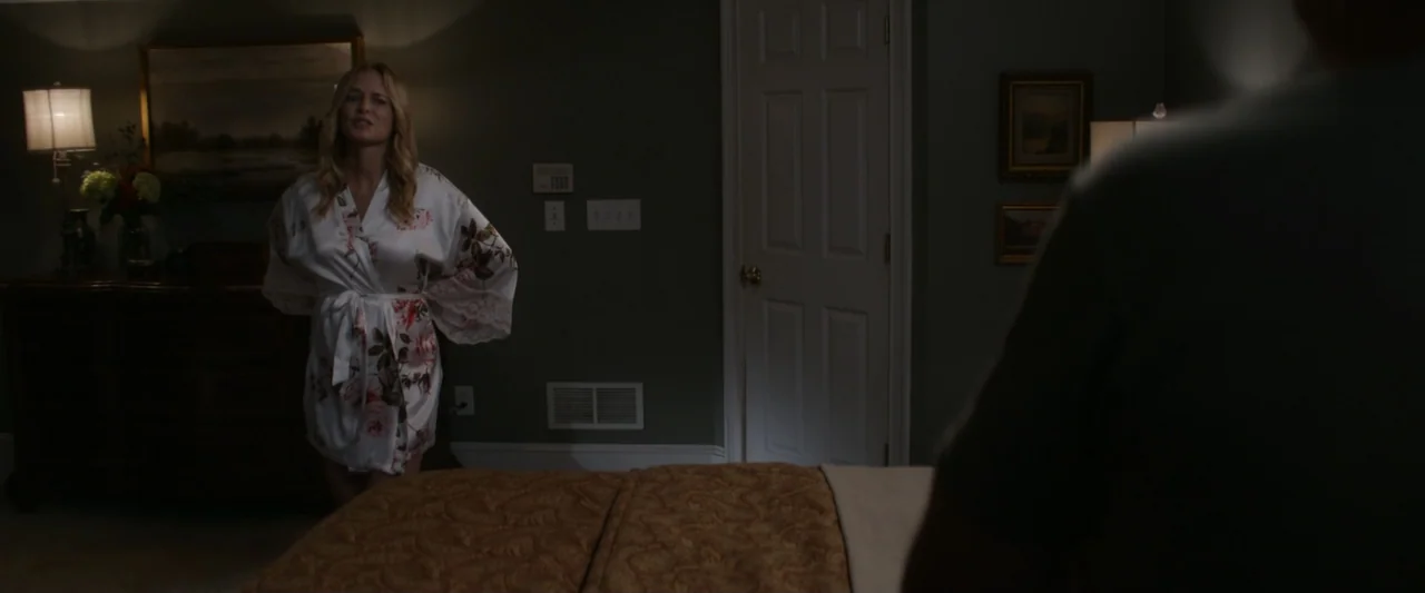 On a Wing and a Prayer (2023) movie still: medium — A dimly lit bedroom features green walls and a white door in the center. A woman in a floral…