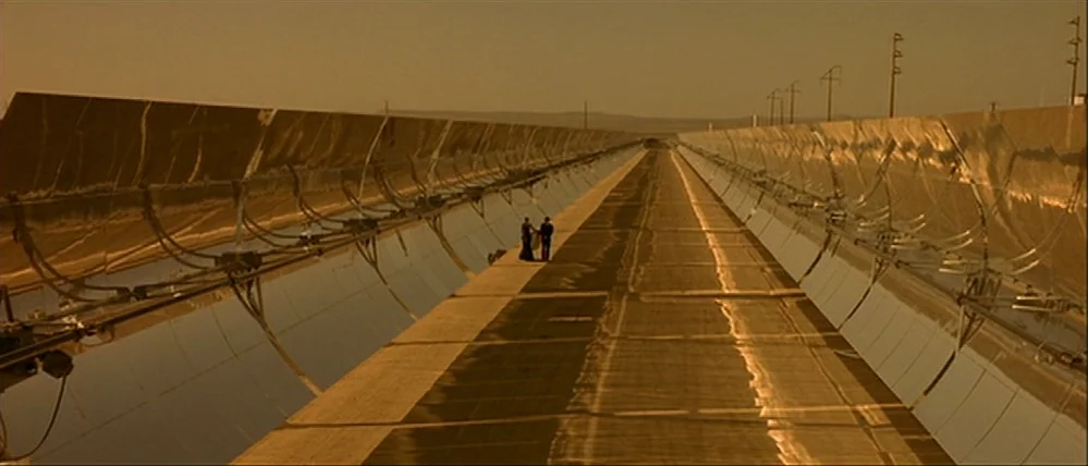 Gattaca (1997) movie still: wide — A vast, industrial solar power plant features endless parallel rows of curved parabolic mirrors. A man and a…