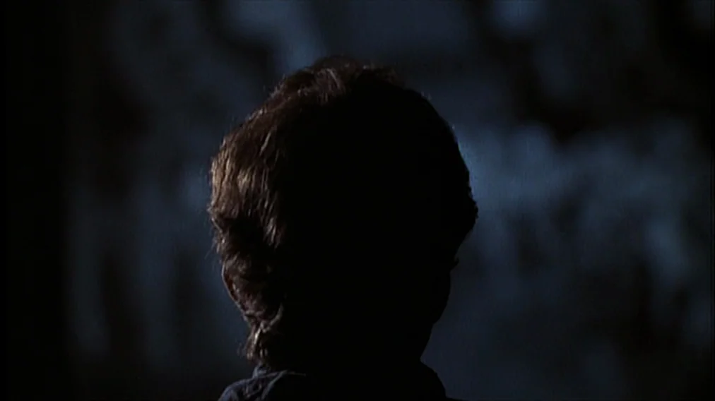 Bonnie And Clyde (1967) movie still: closeup — A dark space features a person positioned against a dim blue background. The subject is shown from…