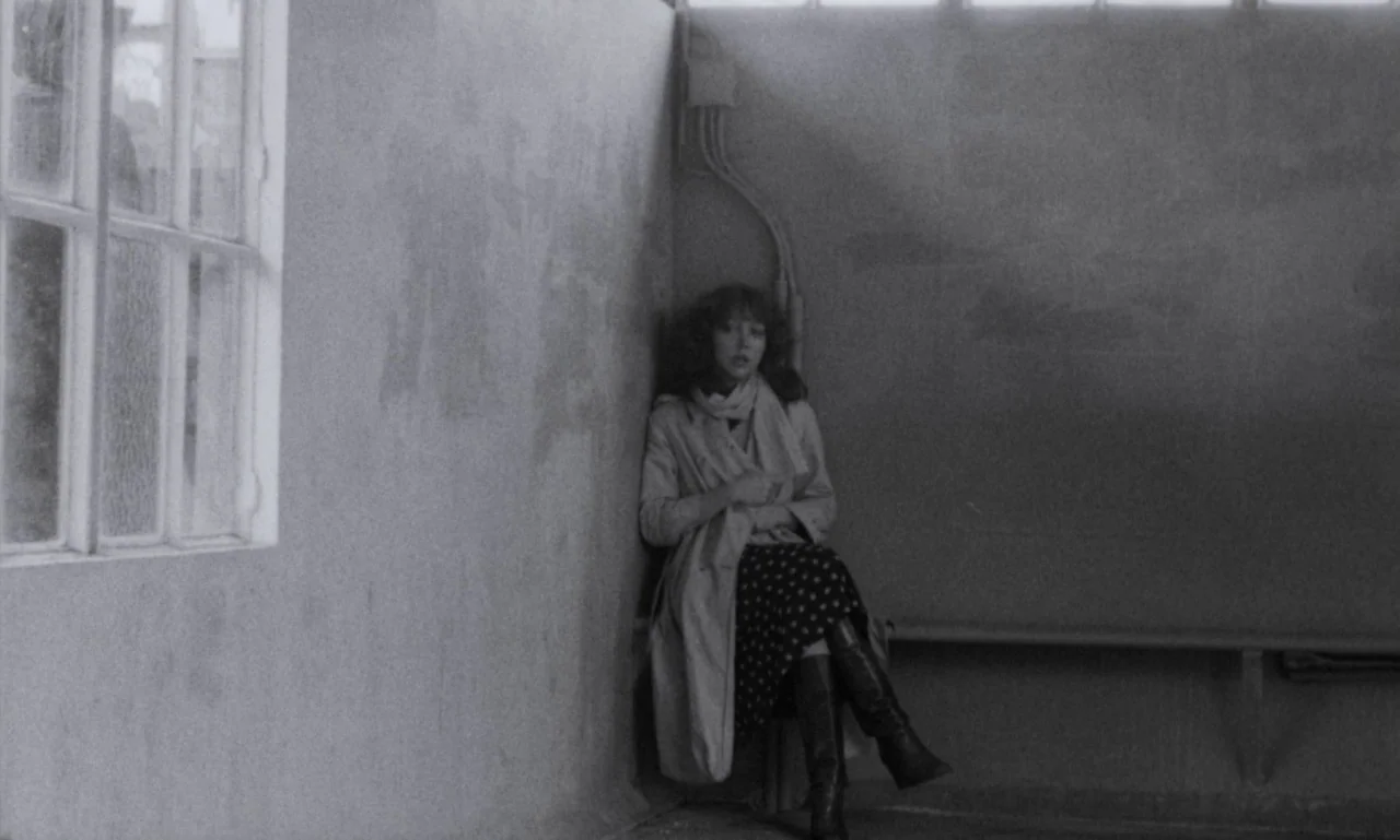 The Secret Son (1979) movie still: fullbody — A spartan bus stop interior features concrete walls and a simple wooden bench seat. A lone woman rests…