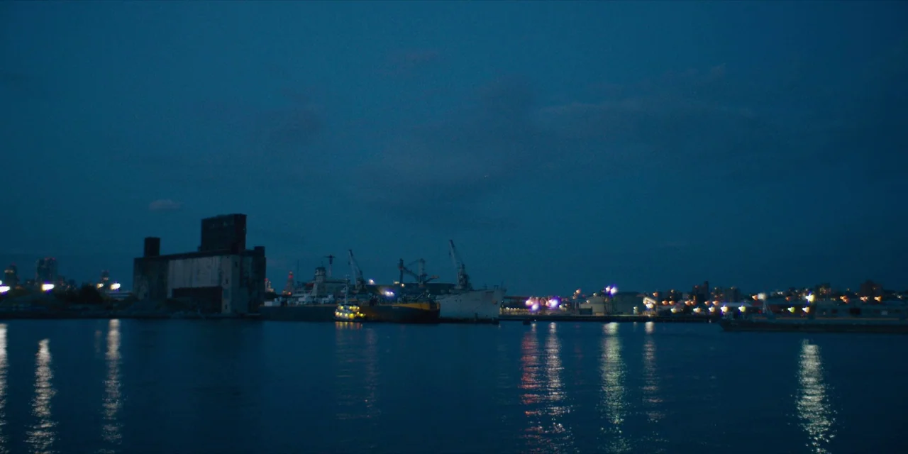 Hearts Beat Loud (2018) movie still: wide — An industrial waterfront at night features large shipping vessels moored near a dark warehouse.…