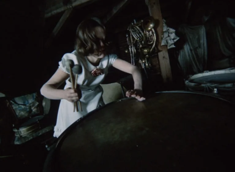 Fruit of Paradise (1970) movie still: medium — A dark, cluttered wooden space with exposed beams and various musical instruments. A young girl in a…