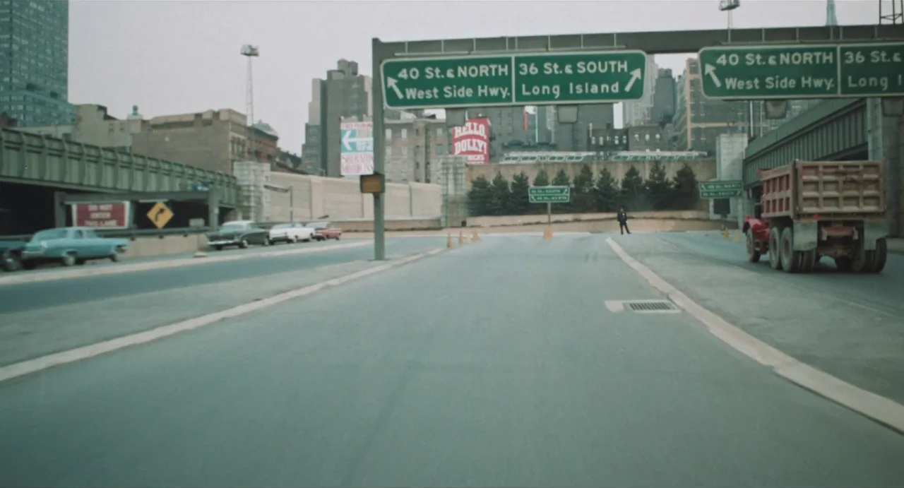 The Rain People (1969) movie still: establishing — An urban highway interchange in New York City with large green metal signage above. A red dump…