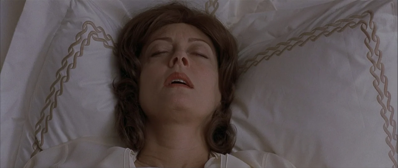 Igby Goes Down (2002) movie still: closeup — A woman lies on a white pillow with embroidered gold chain-link patterns. She is supine and motionless…