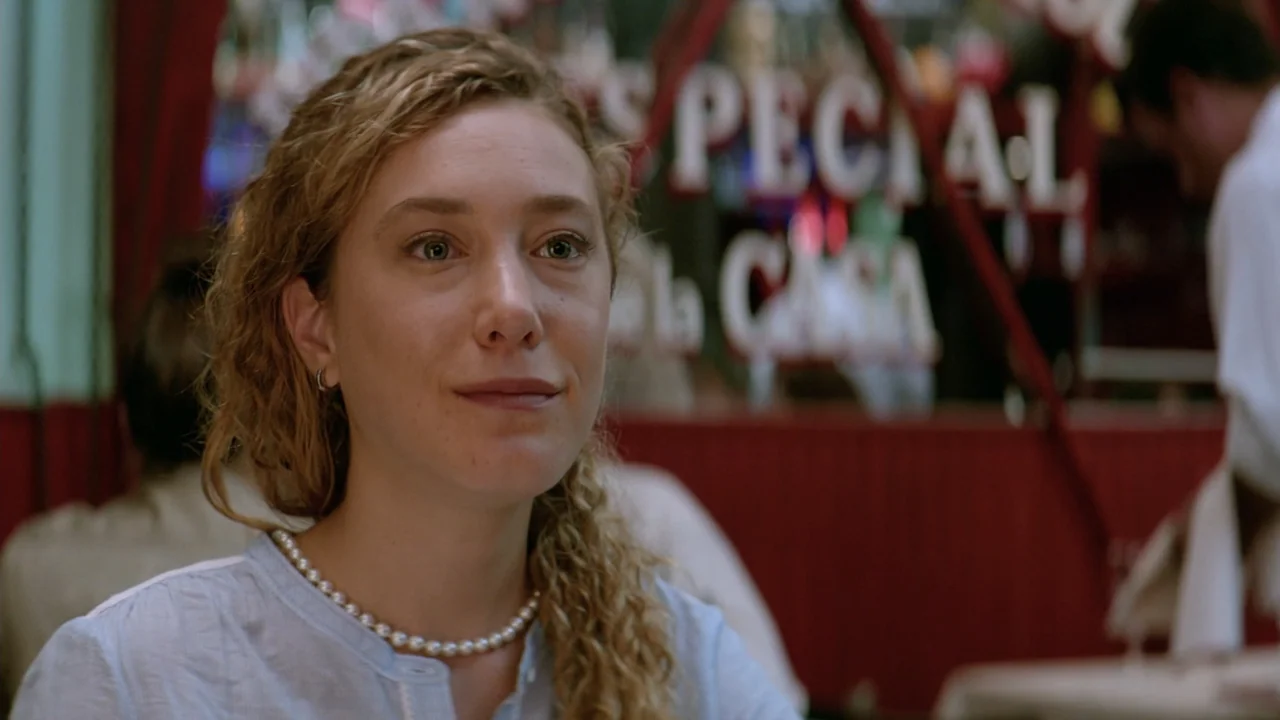 That's Not Cheating (2016) movie still: closeup — A woman sits at a table inside a dimly lit restaurant at night. She gazes slightly off-camera with…